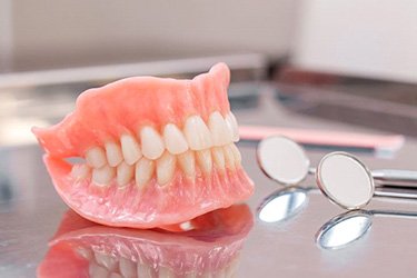 Set of full dentures next to dental mirror