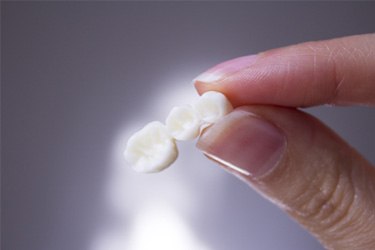 Manicured fingers holding three-unit dental bridge