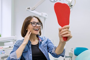 Happy patient using mirror to admire the results of her cosmetic dental treatment