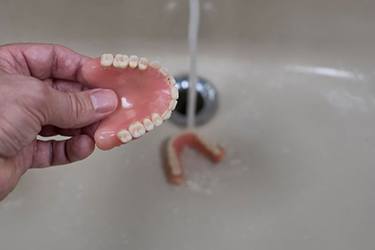 Person rinsing their dentures in sink