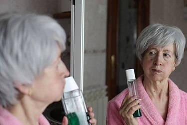 Older woman using mouthwash in front of mirror