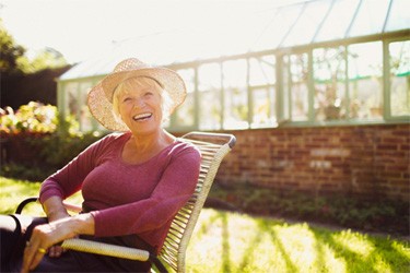Older woman sitting outside, glad to have implant dentures