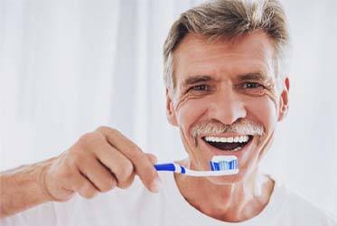 Smiling man brushing his dental implants in Schenectady