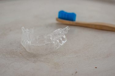 Invisalign aligner next to blue toothbrush on countertop