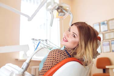 Happy patient in dentist’s chair smiling after cosmetic treatment