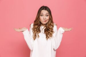 Shrugging woman standing against pink background 