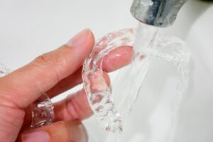 Person rinsing Invisalign retainer under faucet