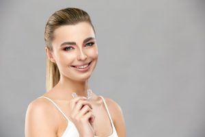 blond woman smiling and holding Invisalign in Capital District