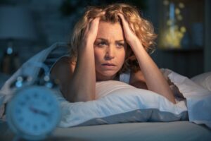  Woman awake in her bed, wearing anxious facial expression 
