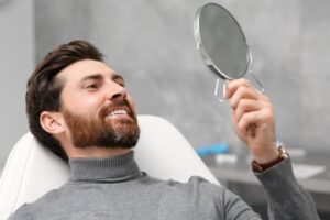 Dental patient holding mirror, admiring his new crown