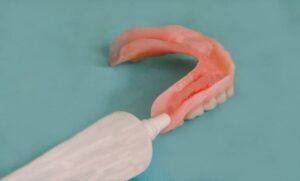 Denture and tube of adhesive