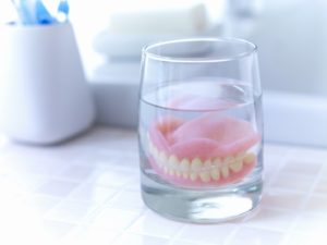 Dentures sitting in glass of water on countertop