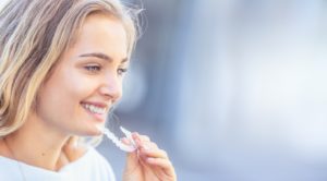 Woman placing aligner in mouth to meet Invisalign wear time